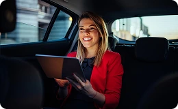 Smiling woman in red using a tablet during a chauffeured birthday or anniversary ride.