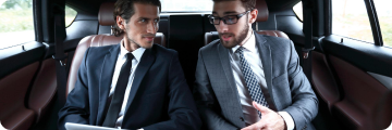  Two business professionals discussing documents in the backseat of a black premium vehicle.