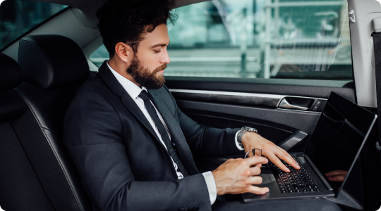Business professional in a black suit working on a laptop in the backseat of a luxury car during transit.