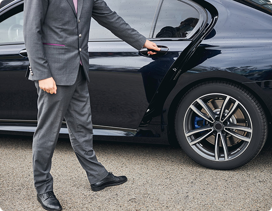 Side profile of a suited chauffeur opening a sleek black sedan, highlighting elegance and professionalism.