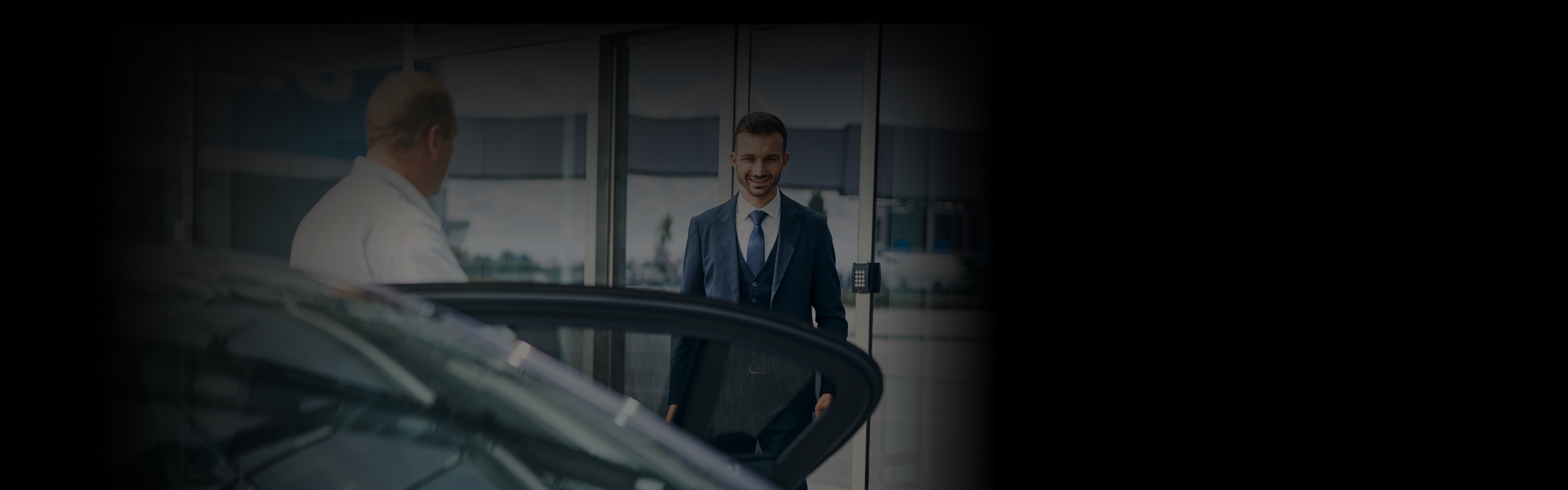 Chauffeur holding the car door open for a smiling business traveler in a suit outside a modern NYC airport terminal