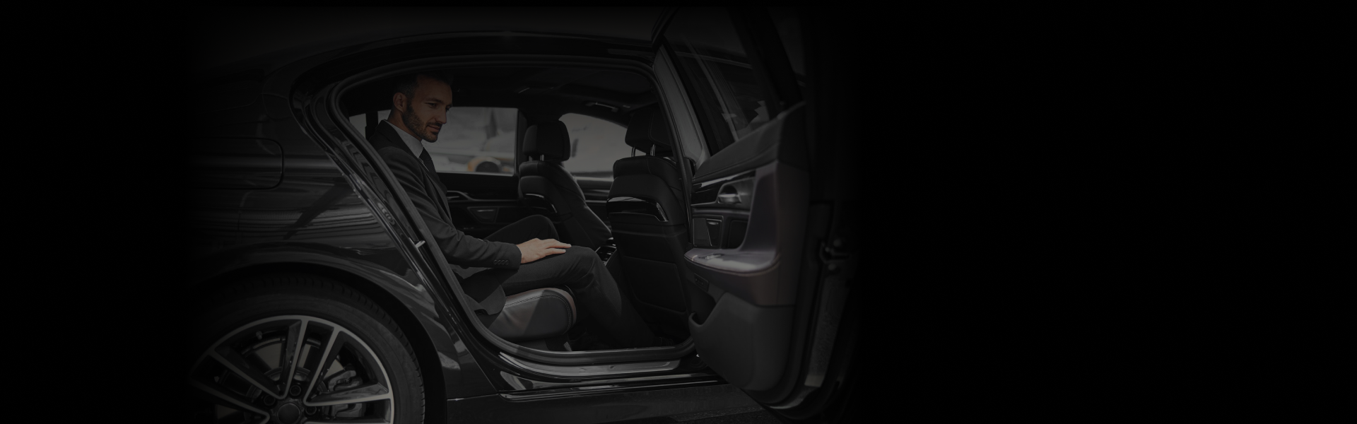 Business traveler in a suit sitting comfortably in the rear seat of a luxury black vehicle with the door open, preparing for a ride