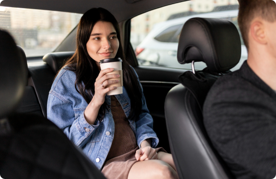 Young woman in a denim jacket enjoying a coffee while sitting comfortably in the backseat of a chauffeured vehicle