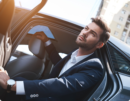 A stylish man in a navy suit steps out of a sleek black car, urban skyline softly reflecting off the door.