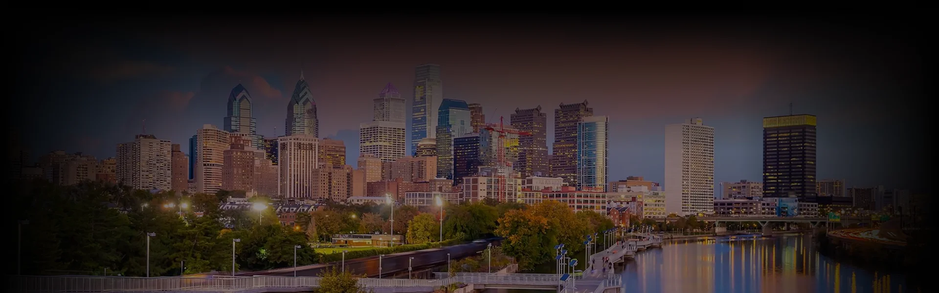 A chauffeur in a black suit opens the door of a black luxury sedan for a client in a cream-colored coat, photographed from above on a cobblestone driveway.