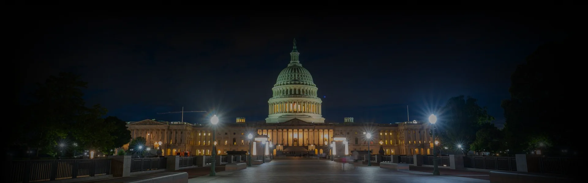 Chauffeur in a black suit opening the door of a black luxury sedan for a client in a cream-colored coat, photographed from above on a cobblestone driveway.